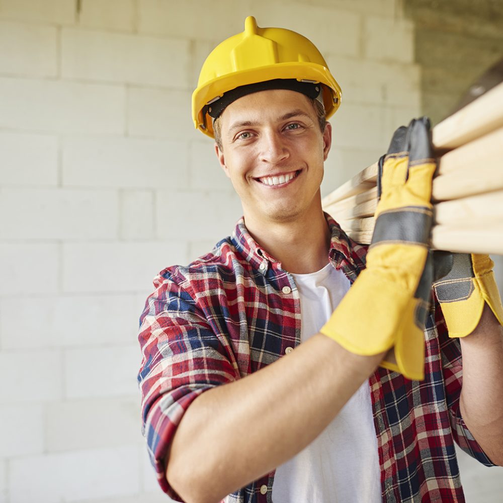 Younger carpenter holds wooden planks